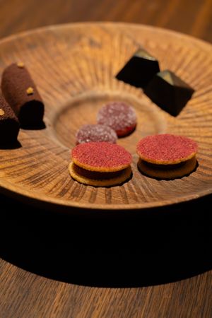 Small round pink-dusted desserts arranged on a textured wooden plate.