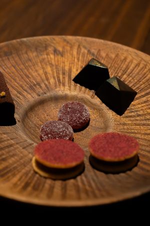 Two circular dessert bites with reddish coating displayed on a rustic wooden plate.