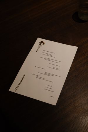 White menu card with elegant typography displayed on dark wooden table surface.