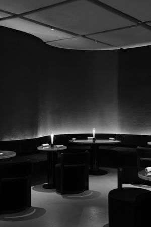 Minimalist dark restaurant interior with circular seating arrangements and subtle lighting.