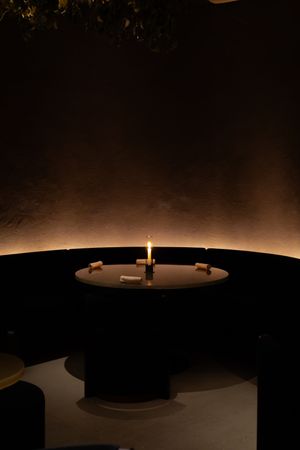 A single lit candle glows in a dark circular dining space creating a dramatic ambiance.