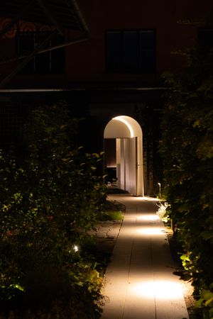 Illuminated garden pathway with glowing archway and landscaping lights creating an inviting nighttime scene.