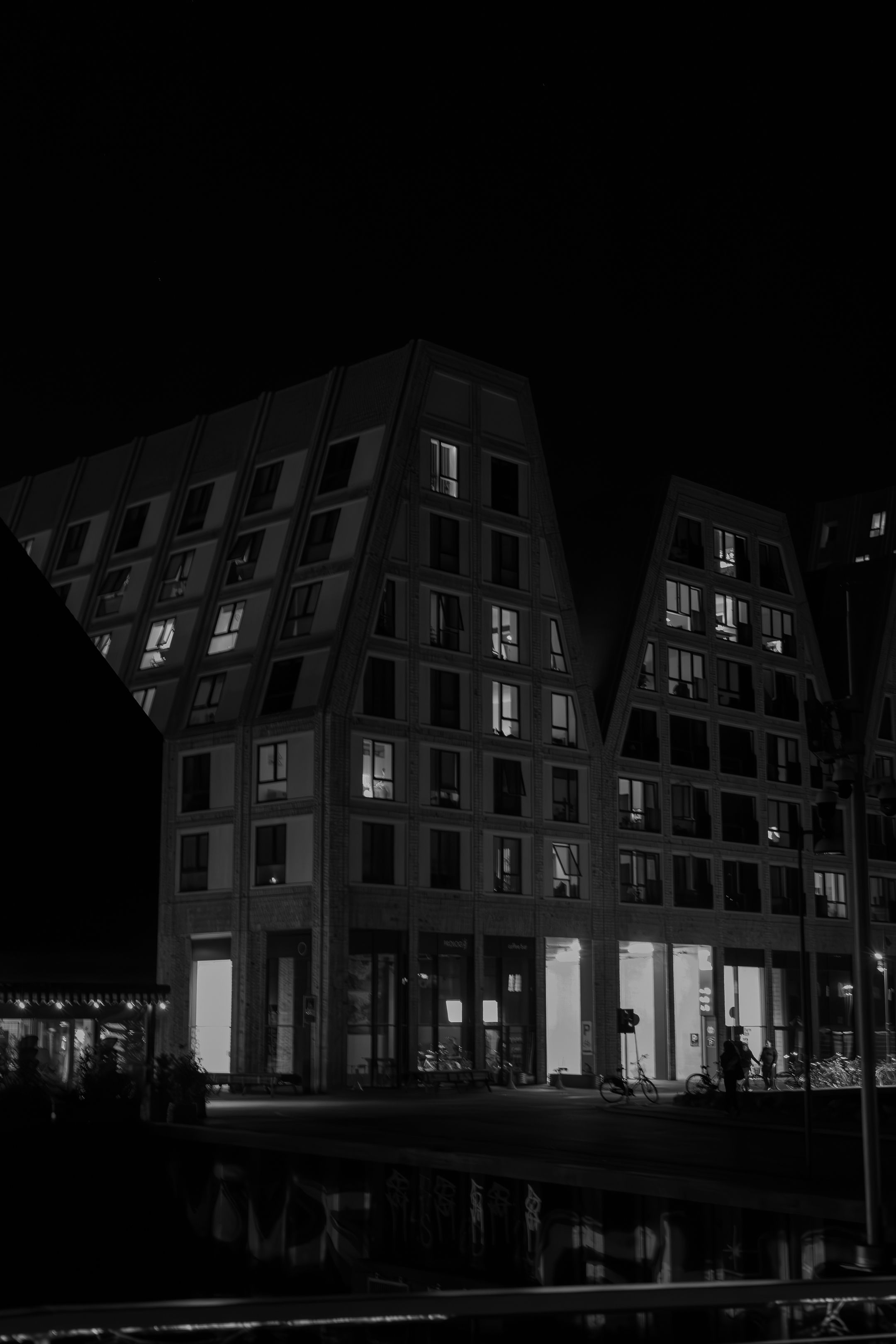 Dark nighttime exterior of a multi-story building with illuminated windows casting light onto the street below.