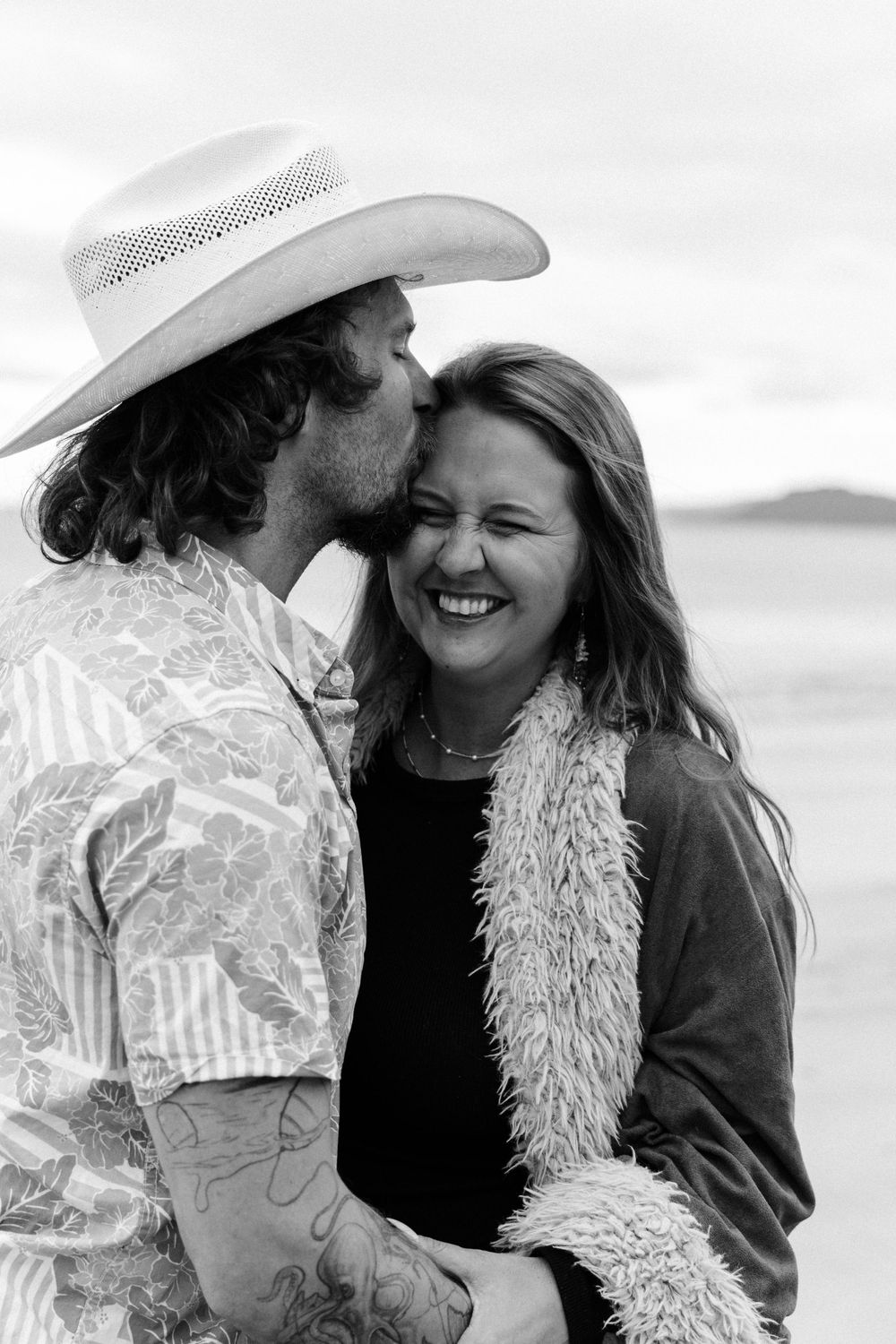 A joyful couple embracing and laughing together in black and white photographs at the seaside.