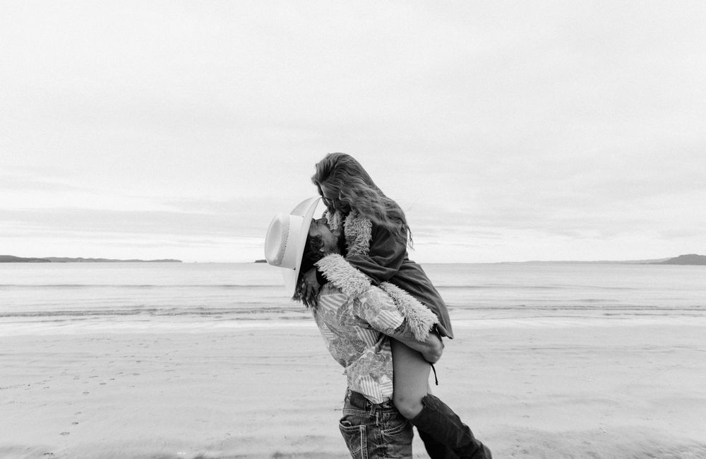 A series of five black and white photographs showing a couple in tender moments at a beach setting.