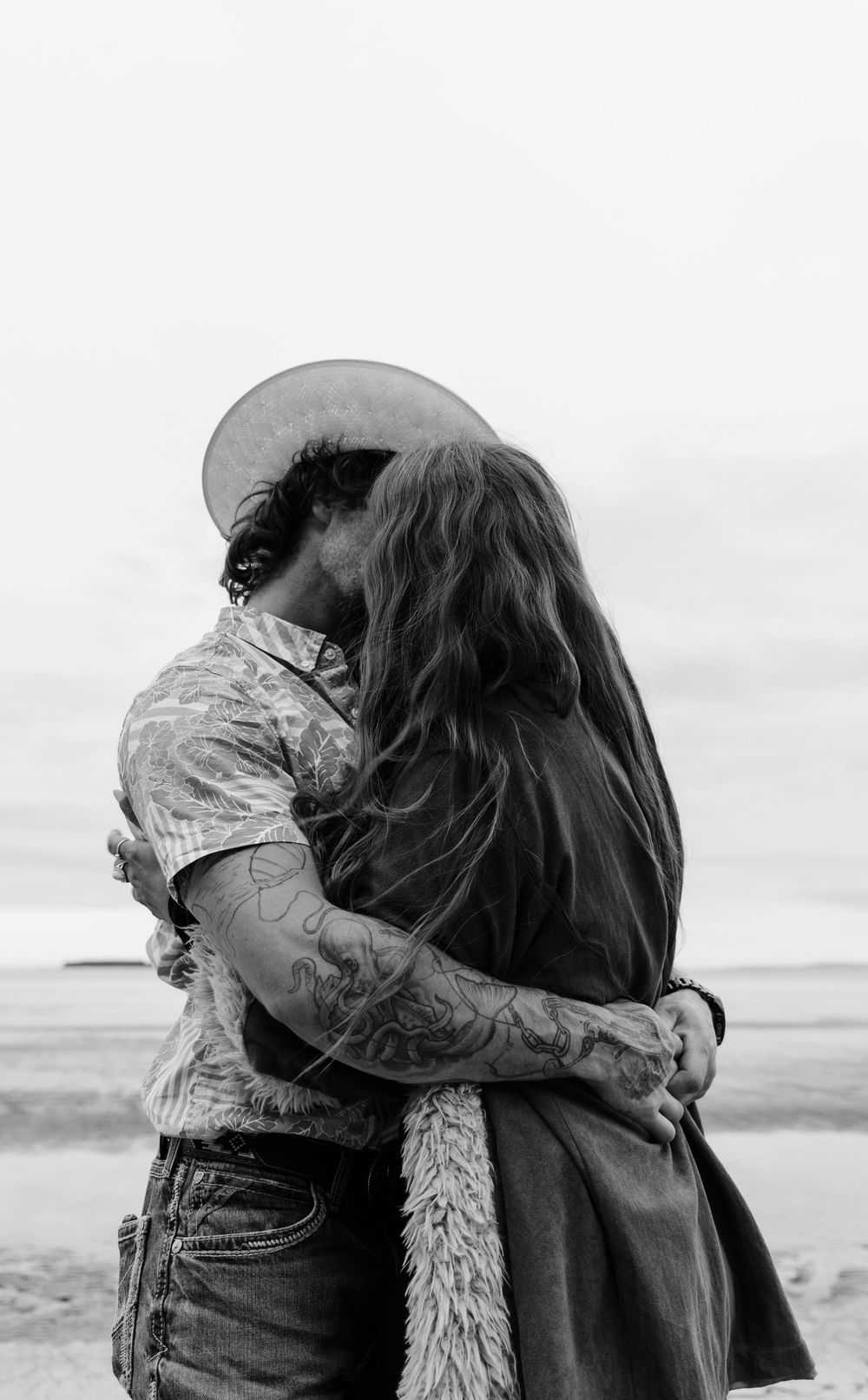 A black and white series showing an intimate moment between a couple on a beach wearing matching jackets.