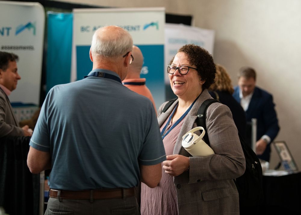 Two professionals networking at a BC Assessment conference, smiling and engaged in conversation at an indoor event.