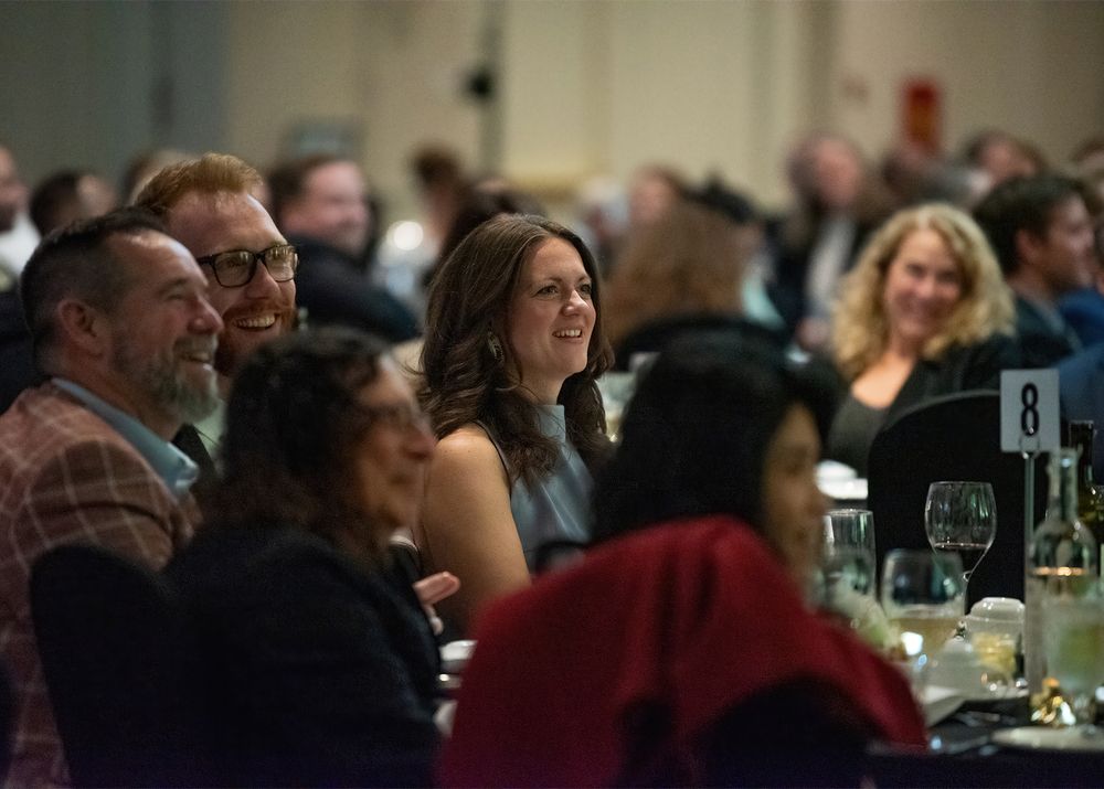 Guests smiling and socializing at a formal banquet event seated at round tables in a large venue.