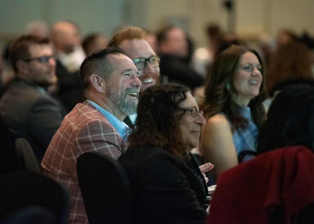 Audience members laughing and smiling during a conference presentation in a crowded event hall.