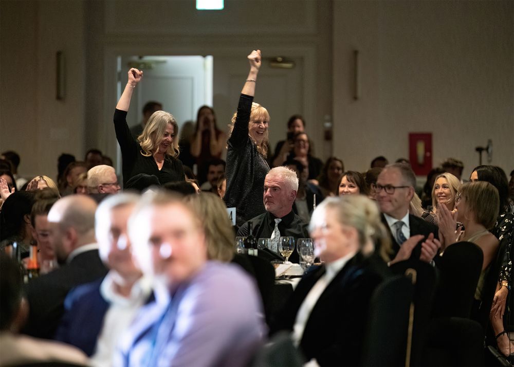 Two happy women walking through audience with fists raised to recieve award - Kelowna event photo by Tania Veitch.