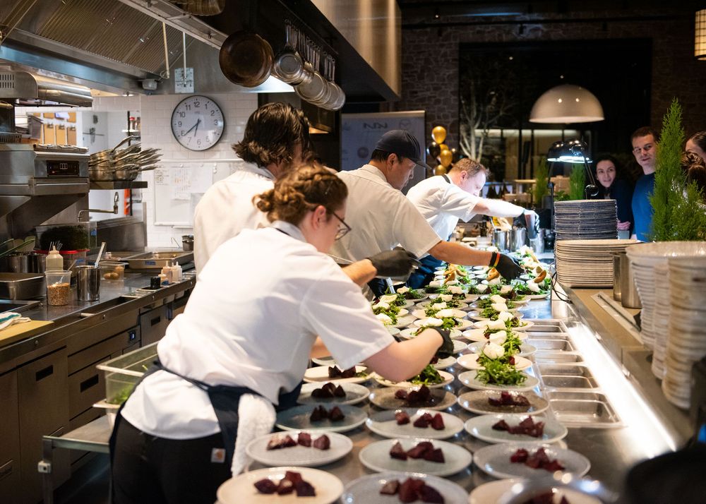 Kitchen staff plating multiple dishes on a long counter during dinner service.
