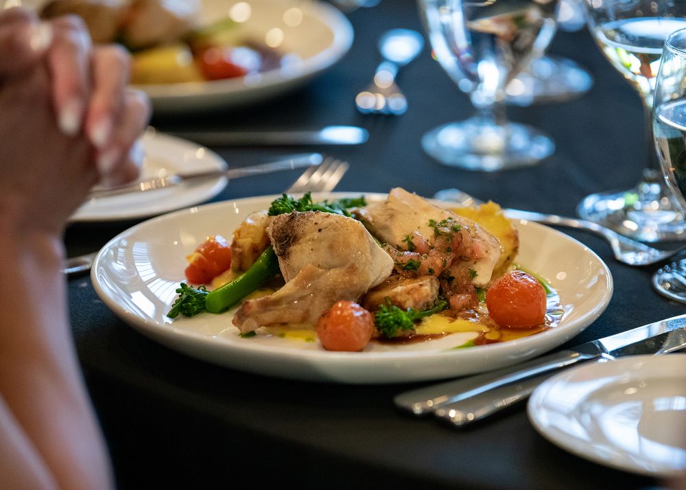 Plate of chicken and vegetables on black tablecloth with guest clasping in anticipation - Kelowna event photo by Tania Veitch.