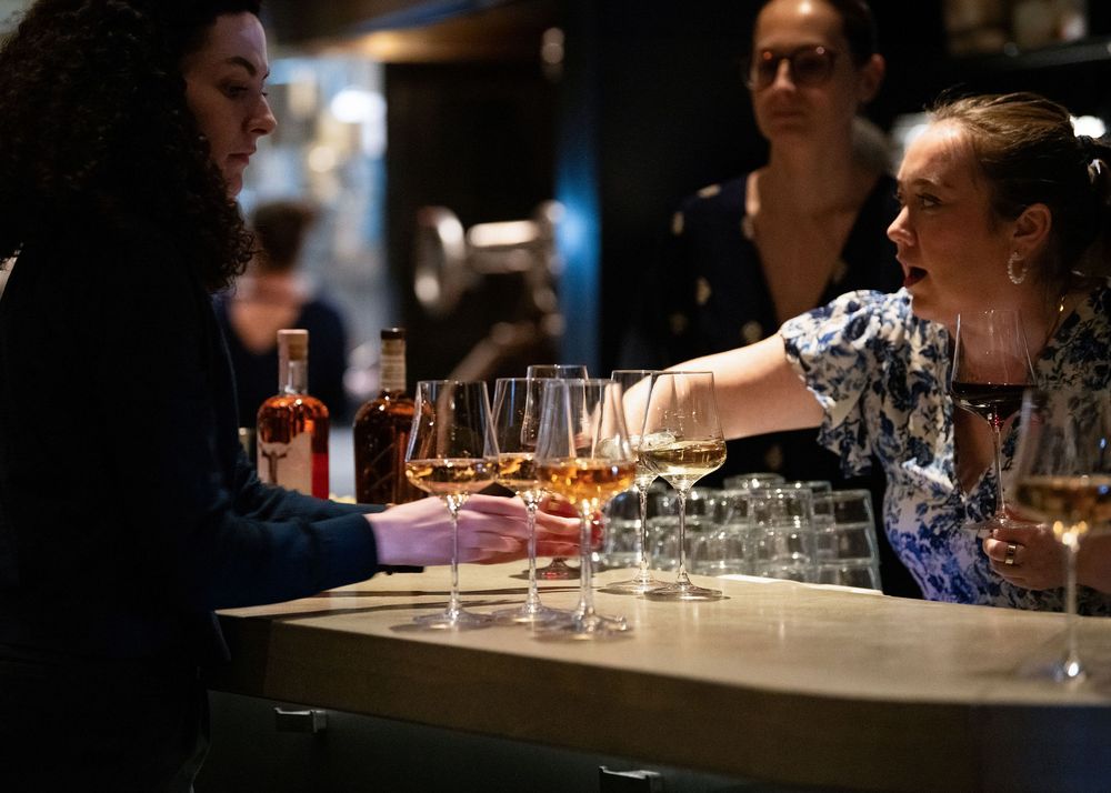 Serving staff handing glasses of wine to guests across a bar during an event.