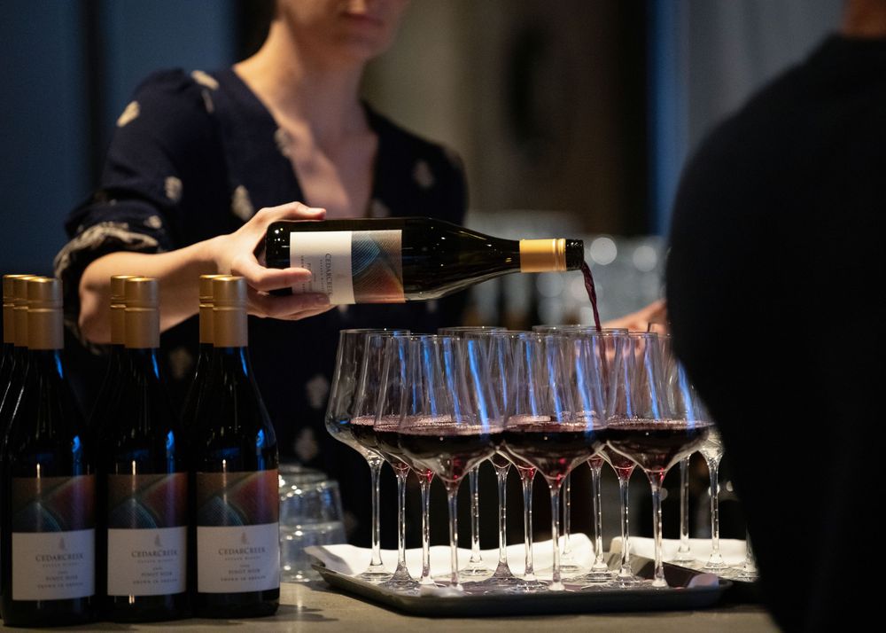 Server pouring red wine into a row of wine glasses at an event bar.
