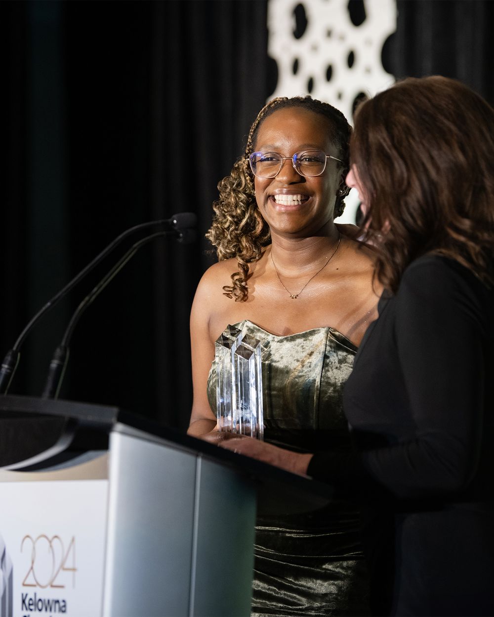 Black woman smiling as she receives award at podium during Kelowna Chamber Business Excellence Awards - photo by Tania Veitch.