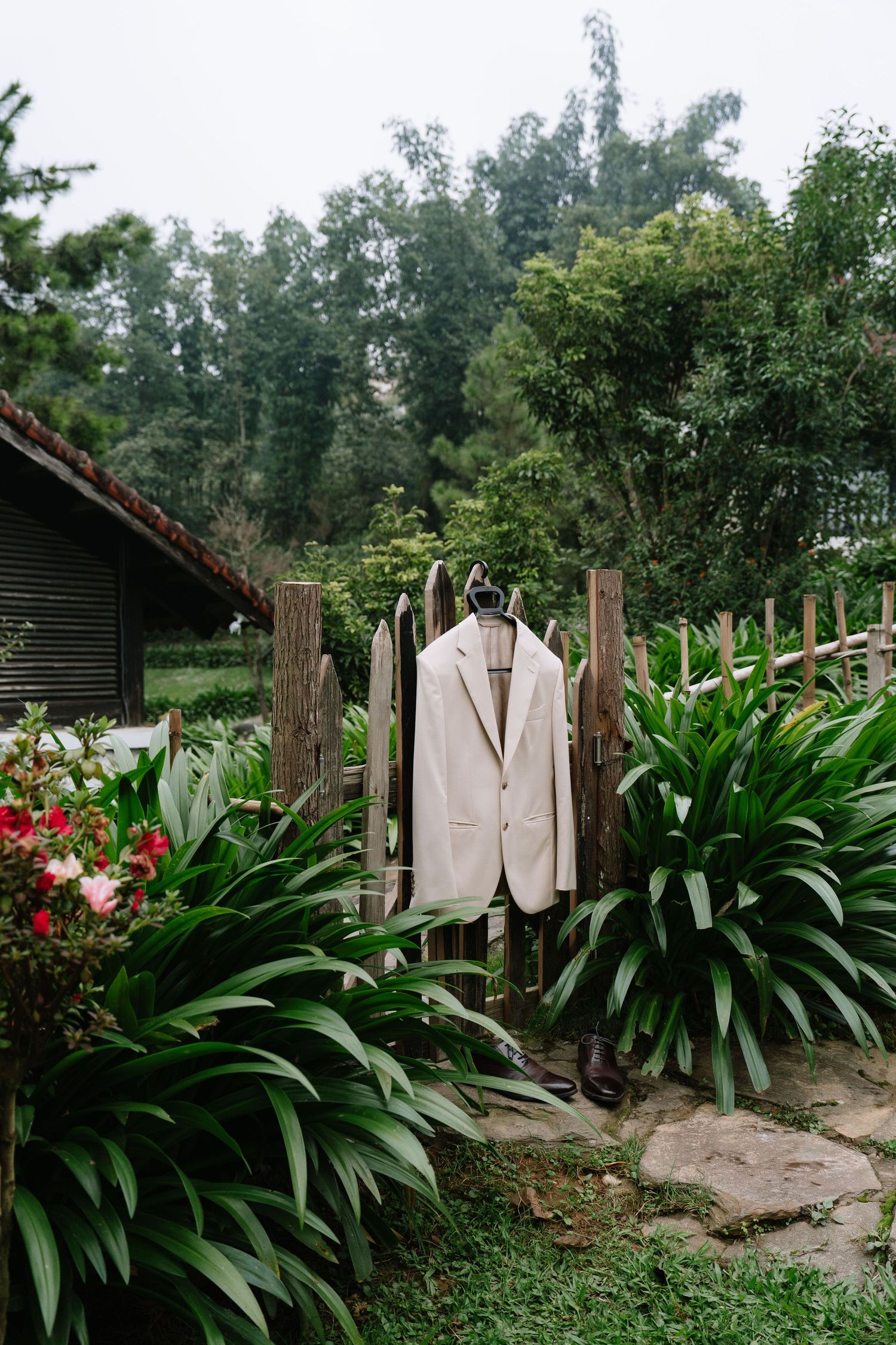White wedding suit jacket hanging on wooden fence surrounded by tropical garden plants.