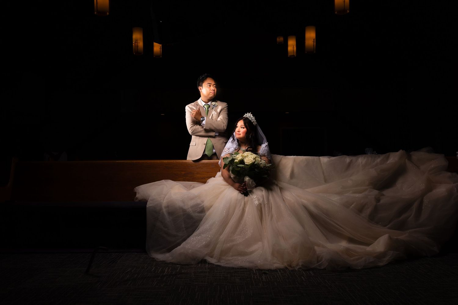 Elegant bridal portrait in a flowing gown against dramatic dark lighting.