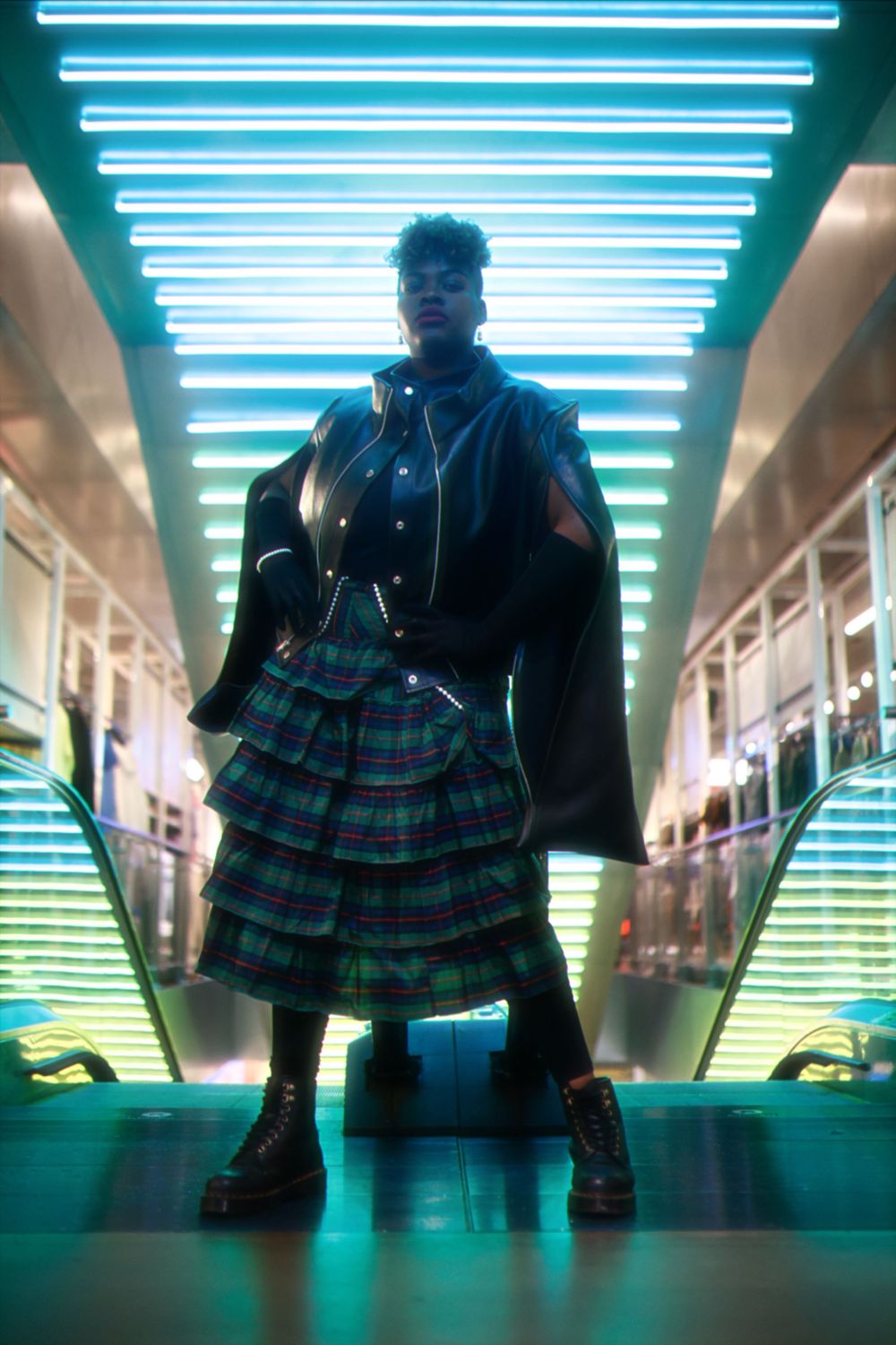 Person wearing a plaid dress stands in a futuristic hallway with glowing blue lights creating a dramatic silhouette.