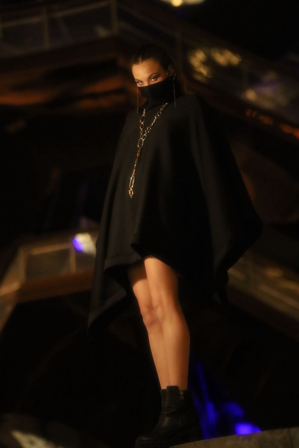 A dark profile silhouette of legs and boots walking across a dimly lit space at night with blue light in the background.