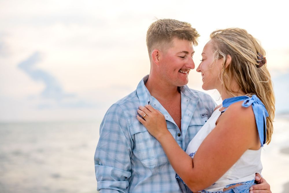 A couple shares romantic moments together during a seaside photoshoot at sunset wearing coordinated blue outfits.