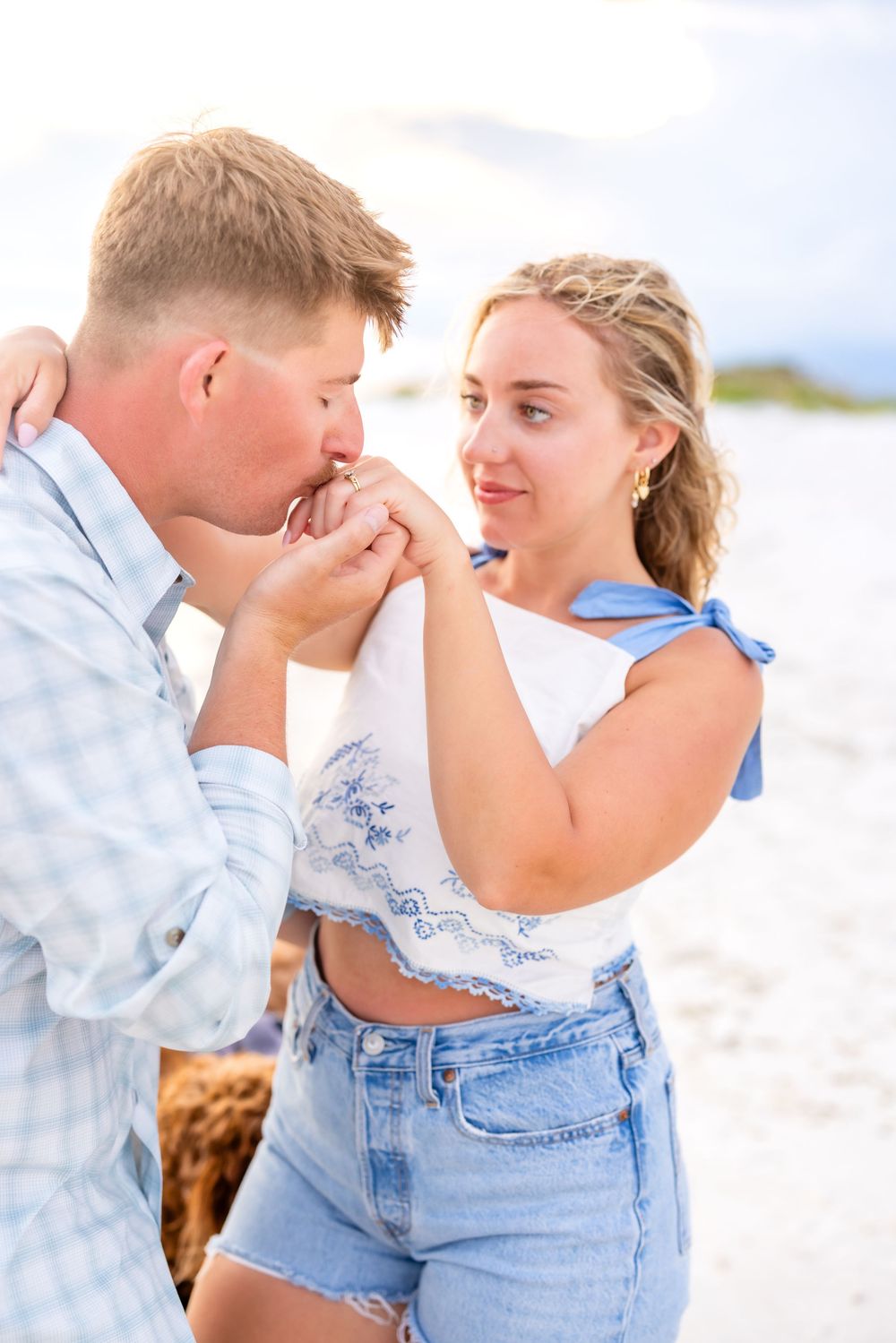 A couple shares a romantic and playful moment together on a bright sandy beach.