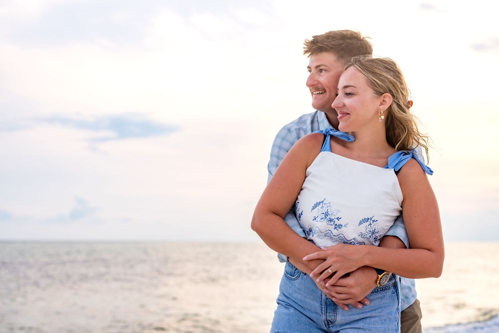 A couple wearing blue and white outfits embraces lovingly on a sunny beach during a photo session.