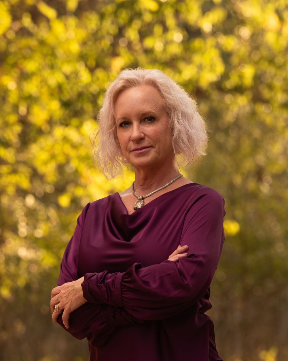 A person wearing a burgundy sweater poses expressively against a blurred yellow autumn background.