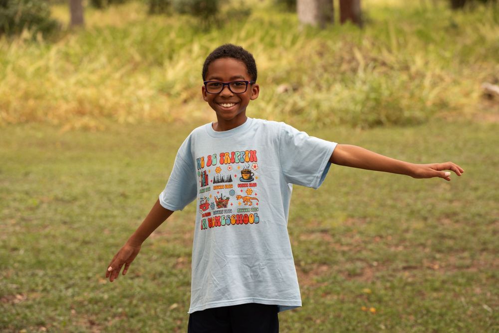 A child wearing a graphic t-shirt smiles and poses in a grassy outdoor setting.
