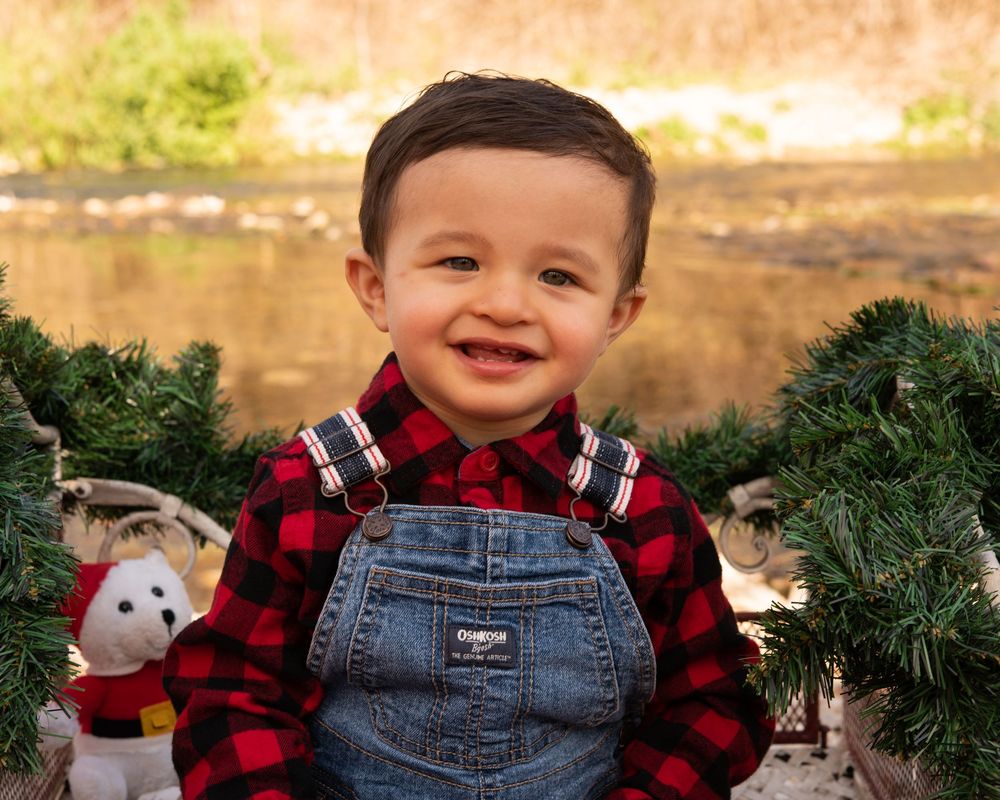 A festive holiday photo banner with plaid shirts, denim overalls, and evergreen decorations against a warm golden backdrop.