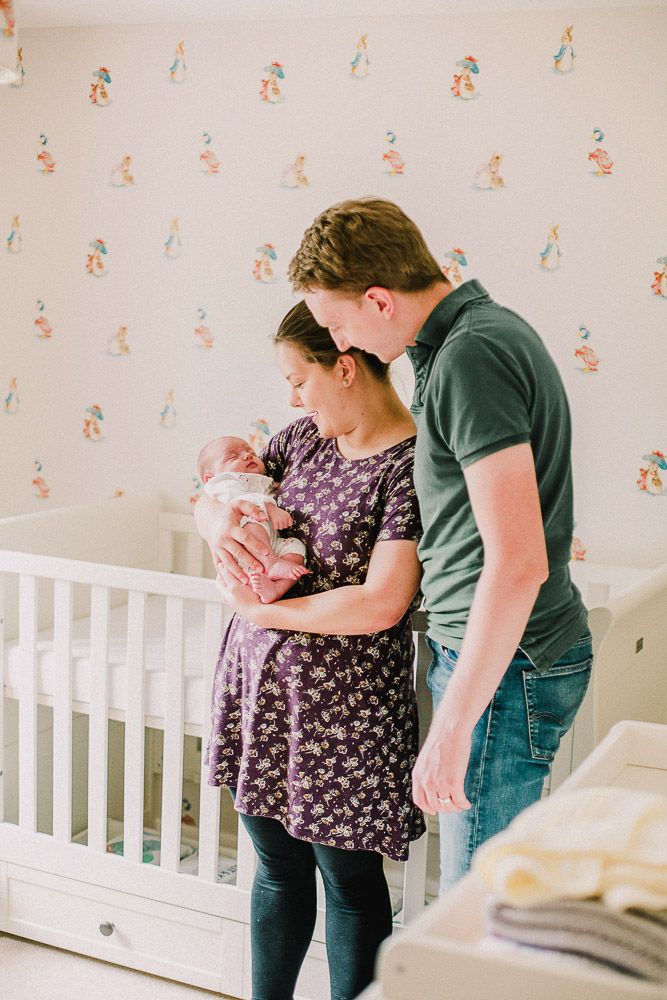 Parents sharing tender moment with newborn baby in nursery with floral wallpaper.