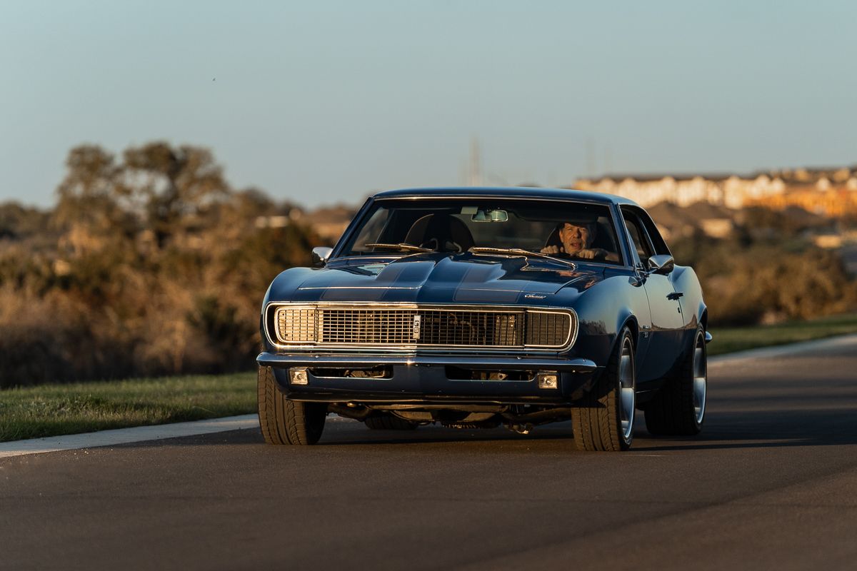 Classic cars lined up on a road during golden hour with dramatic lighting.