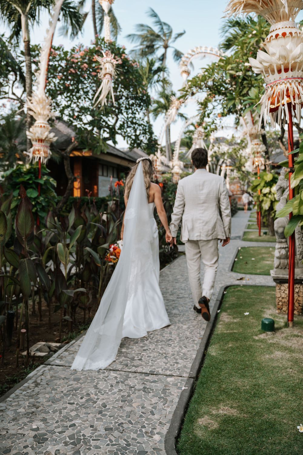 Capturing a couple's walk down a tropical wedding walkway on their wedding day with swaying palm trees and traditional Balinese bamboo decor
