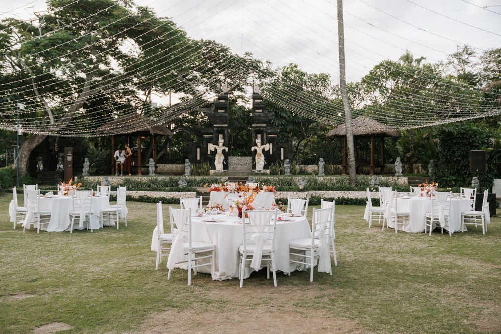 Elegant outdoor wedding reception setup featuring round white tables arranged on a green lawn under string lights.