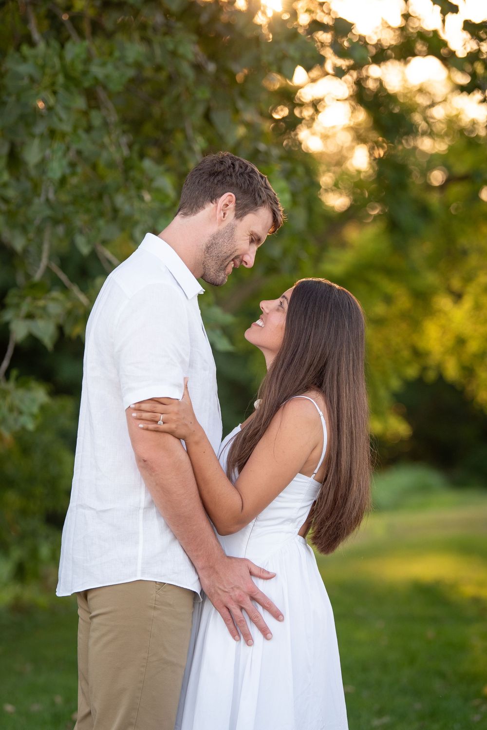 Intimate outdoor portrait session showing couple in white clothing embracing in a park at sunset.
