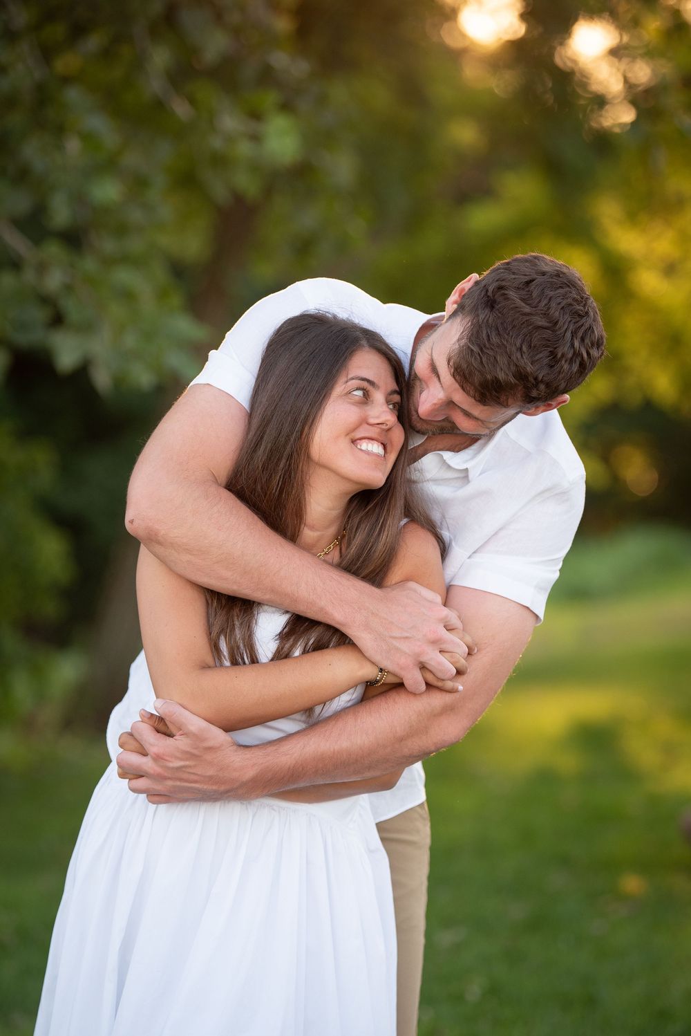 Couple in coordinated white outfits share intimate embrace during golden hour portrait session.