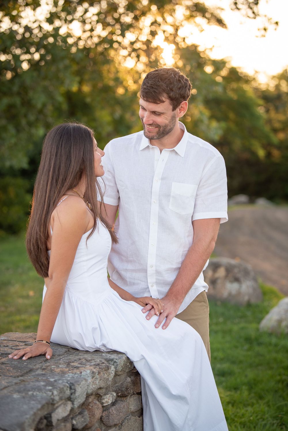 Romantic couple poses on stone wall during sunset outdoor photography session.