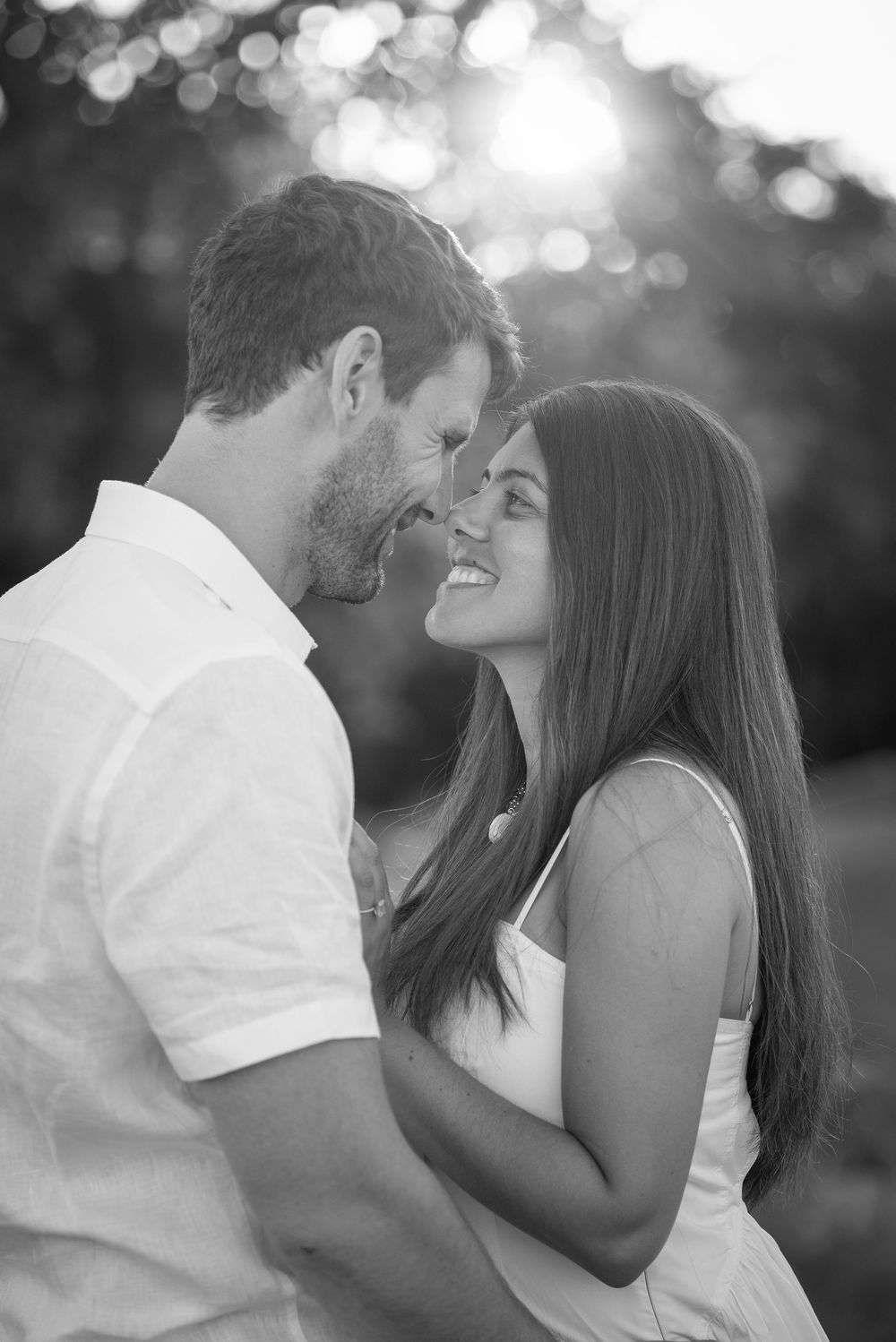 Romantic couple sharing an intimate moment at sunset with bokeh lights in black and white.