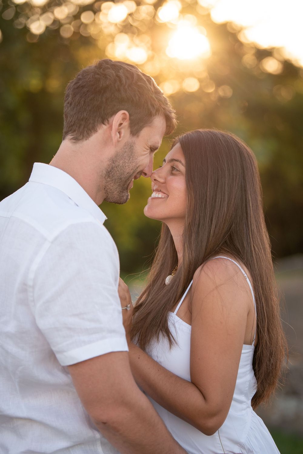 Loving couple embracing outdoors during golden hour with soft bokeh background.