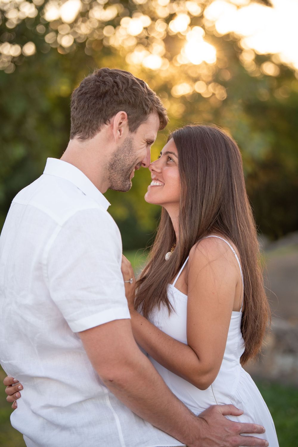 Couple in white clothing sharing tender moment in garden during sunset.