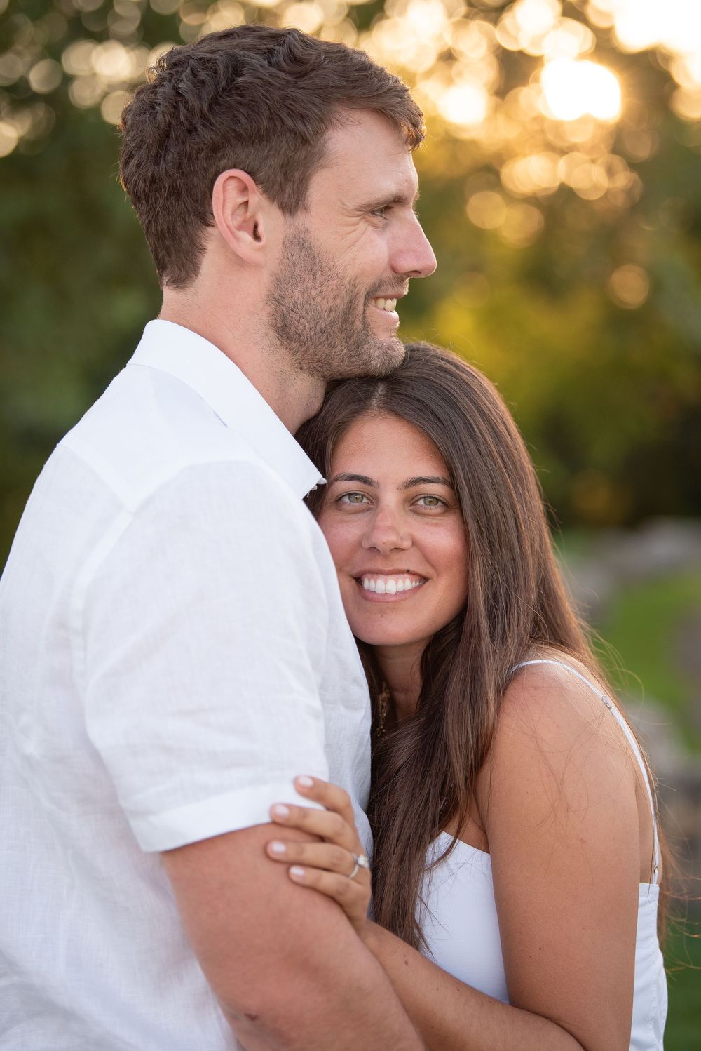 Happy couple embracing outdoors with golden sunlight filtering through trees.