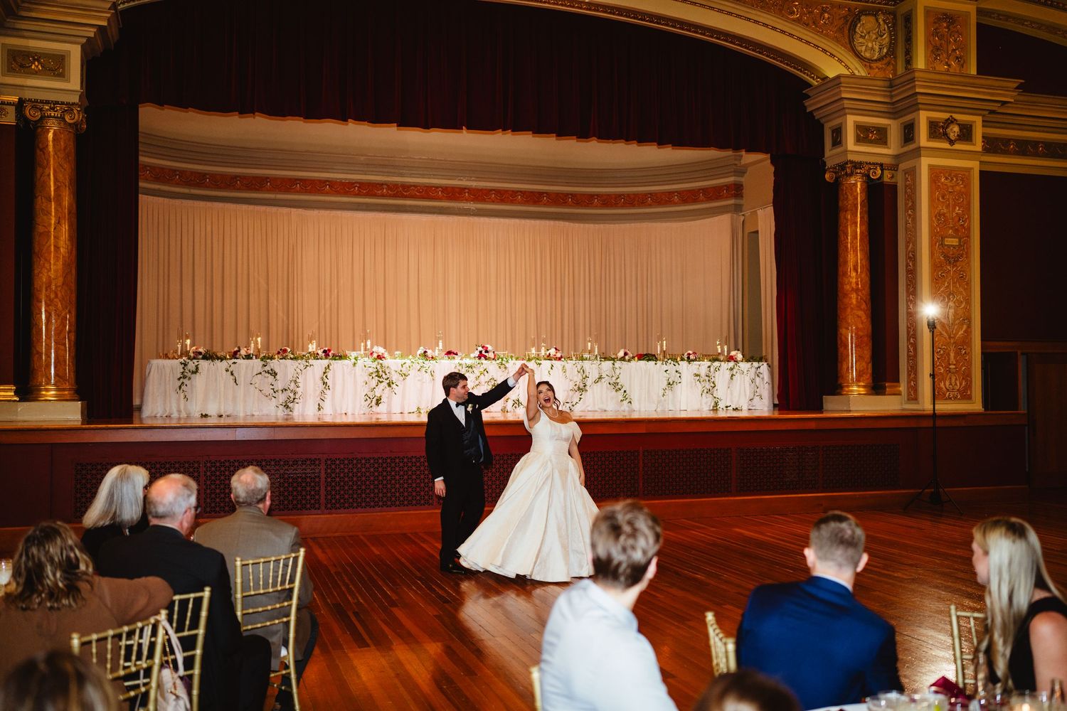 Stage view of an illuminated historic theater with ornate architectural details and curved balcony seating.