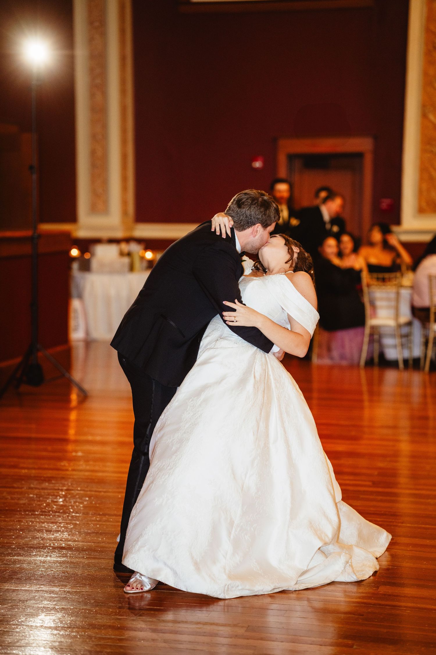 A bride and groom perform a dramatic ballroom dance dip on a polished wooden floor at their wedding reception.