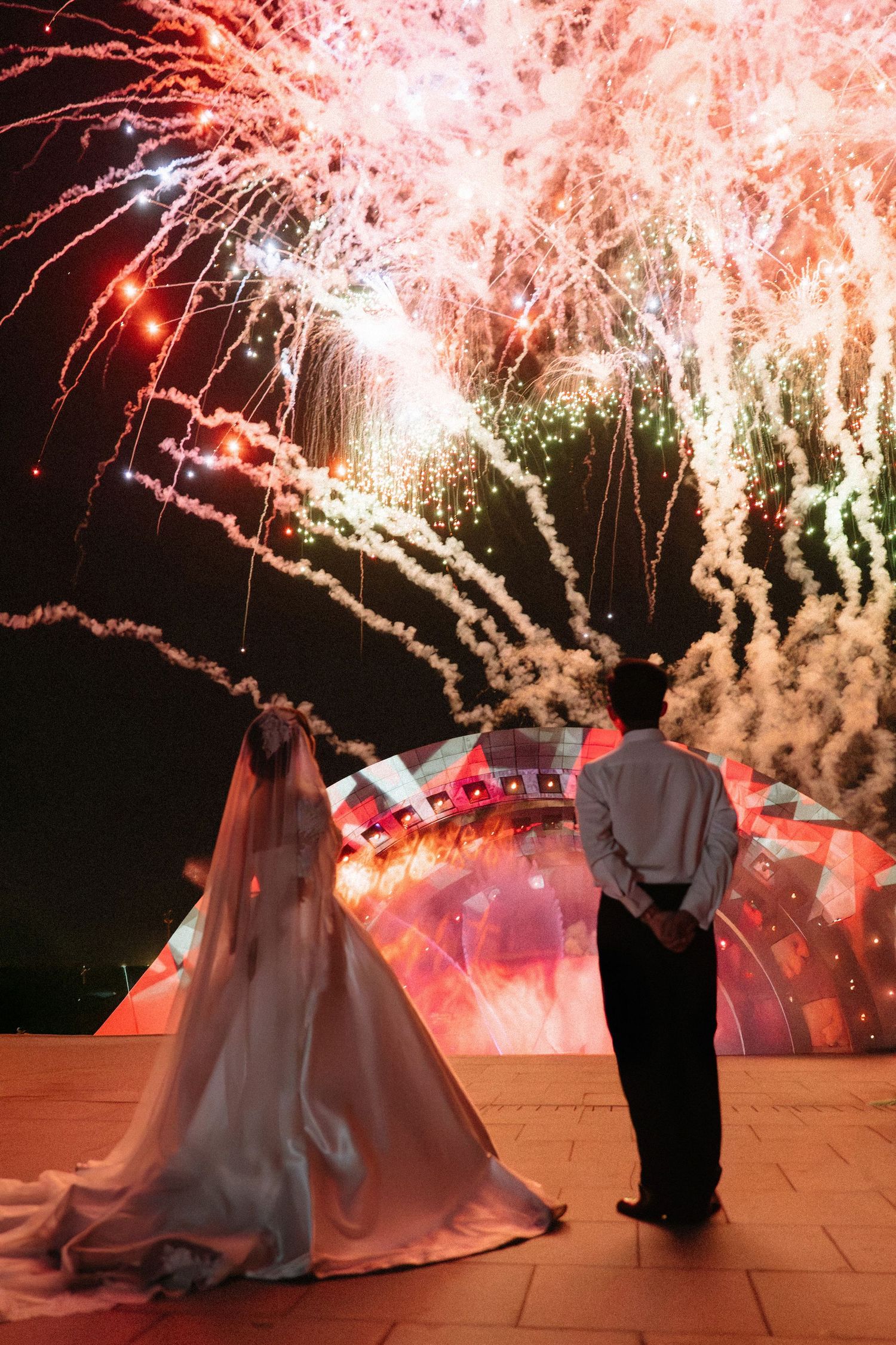 Newlywed couple watching a spectacular fireworks display light up the night sky at their wedding.