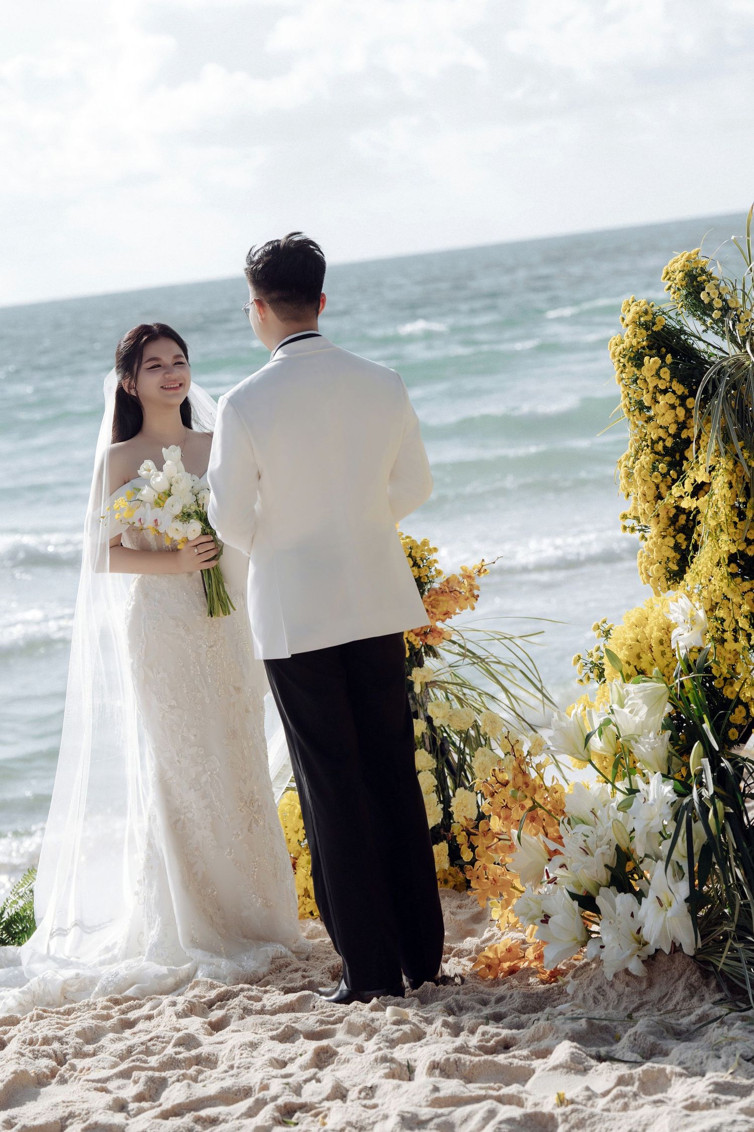 Bride and groom exchange vows at a beach wedding with yellow floral arch.