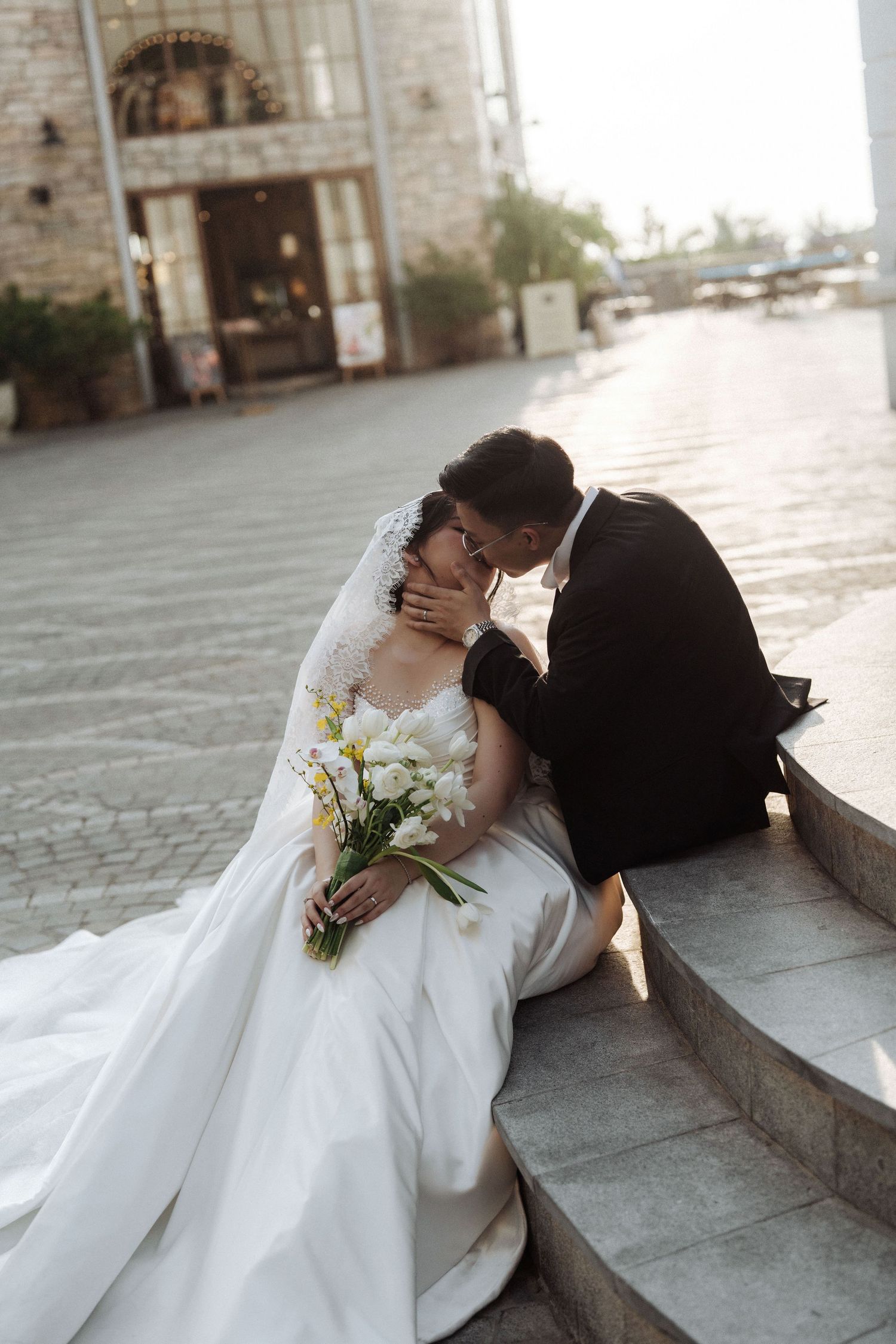 Bride and groom share a romantic moment seated on outdoor steps.