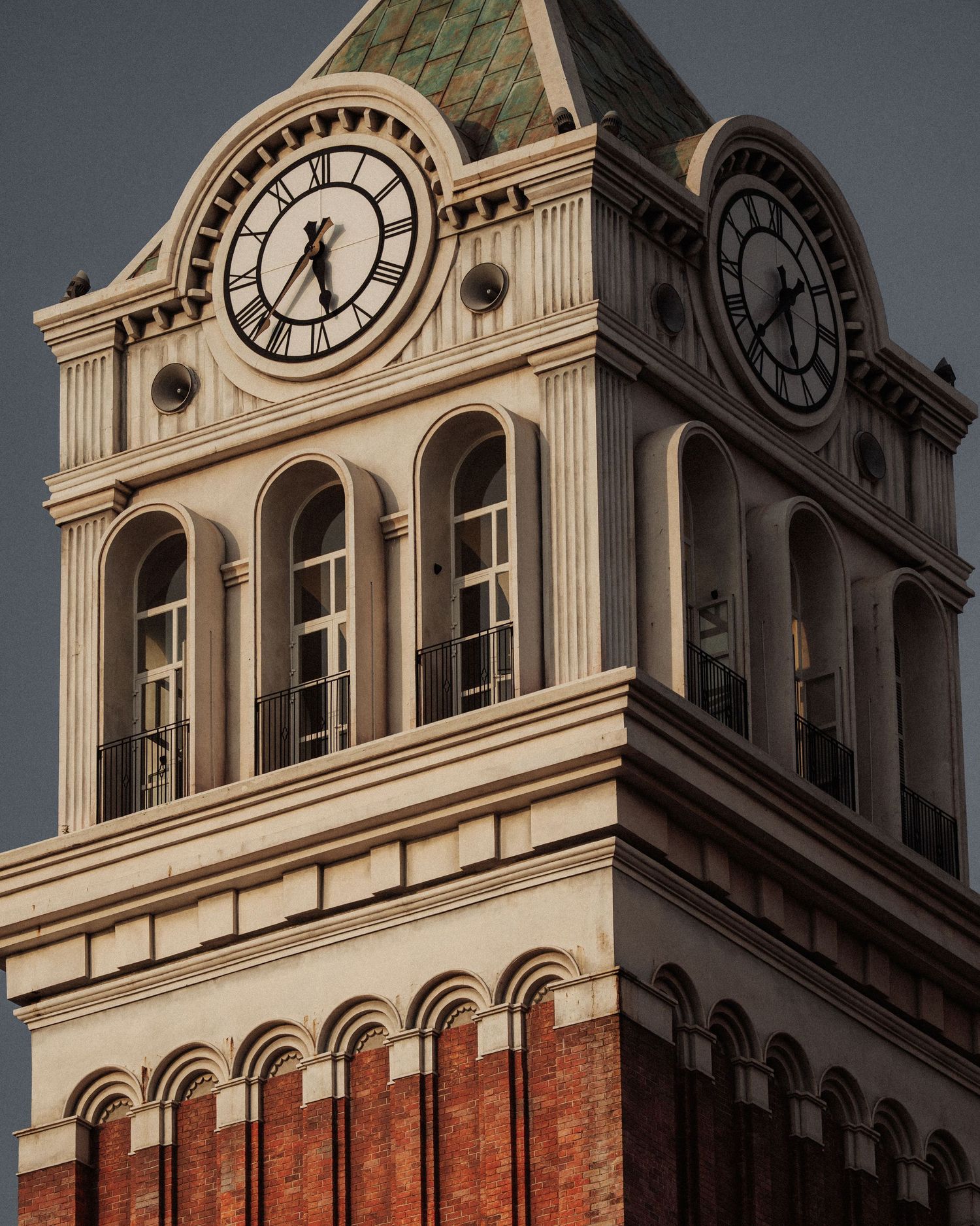 Historic brick clock tower with Roman numeral clock faces at dusk.