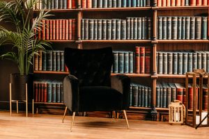Elegant black tufted armchair in front of a wooden bookshelf filled with vintage books in a cozy library.