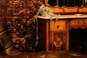 Ornate Victorian antique desk with carved wood details, marble top, and decorative floral arrangement against embossed ceiling tile.
