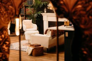 Elegant living room with white armchair, fireplace, bookshelf, and wicker basket on hardwood floors.