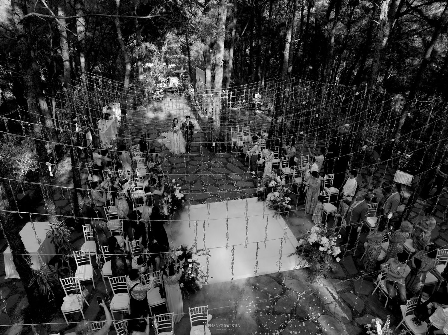 Black and white aerial view inside glass forest wedding chapel with rows of chairs and geometric decor.